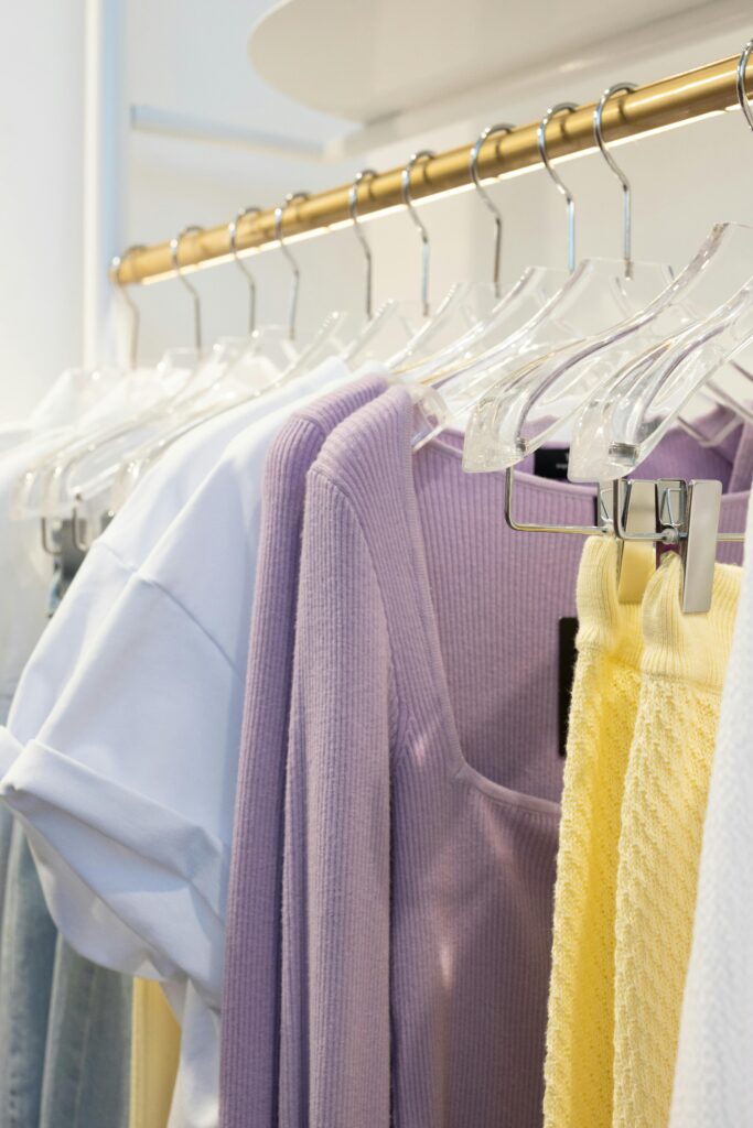 A collection of pastel-colored clothes hanging on a gold wardrobe rack in an indoor boutique.